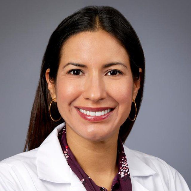 A woman in a white lab coat is smiling for the camera