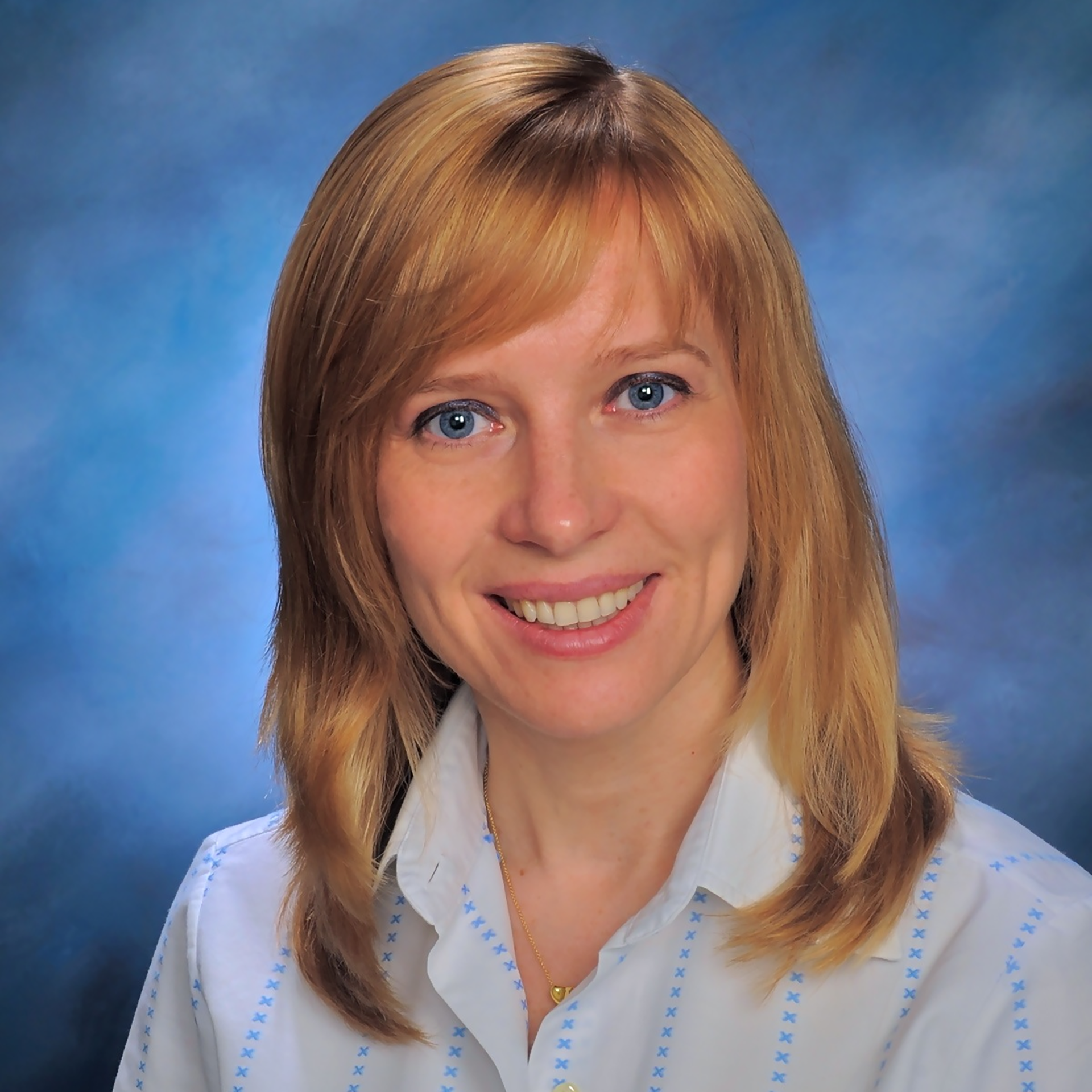 A woman with blonde hair and blue eyes is smiling for the camera