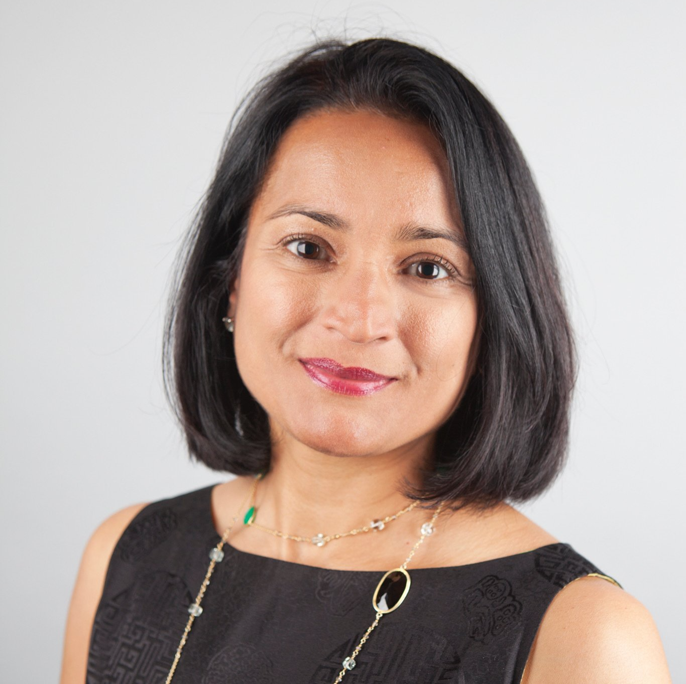 A woman wearing a black dress and a necklace smiles for the camera