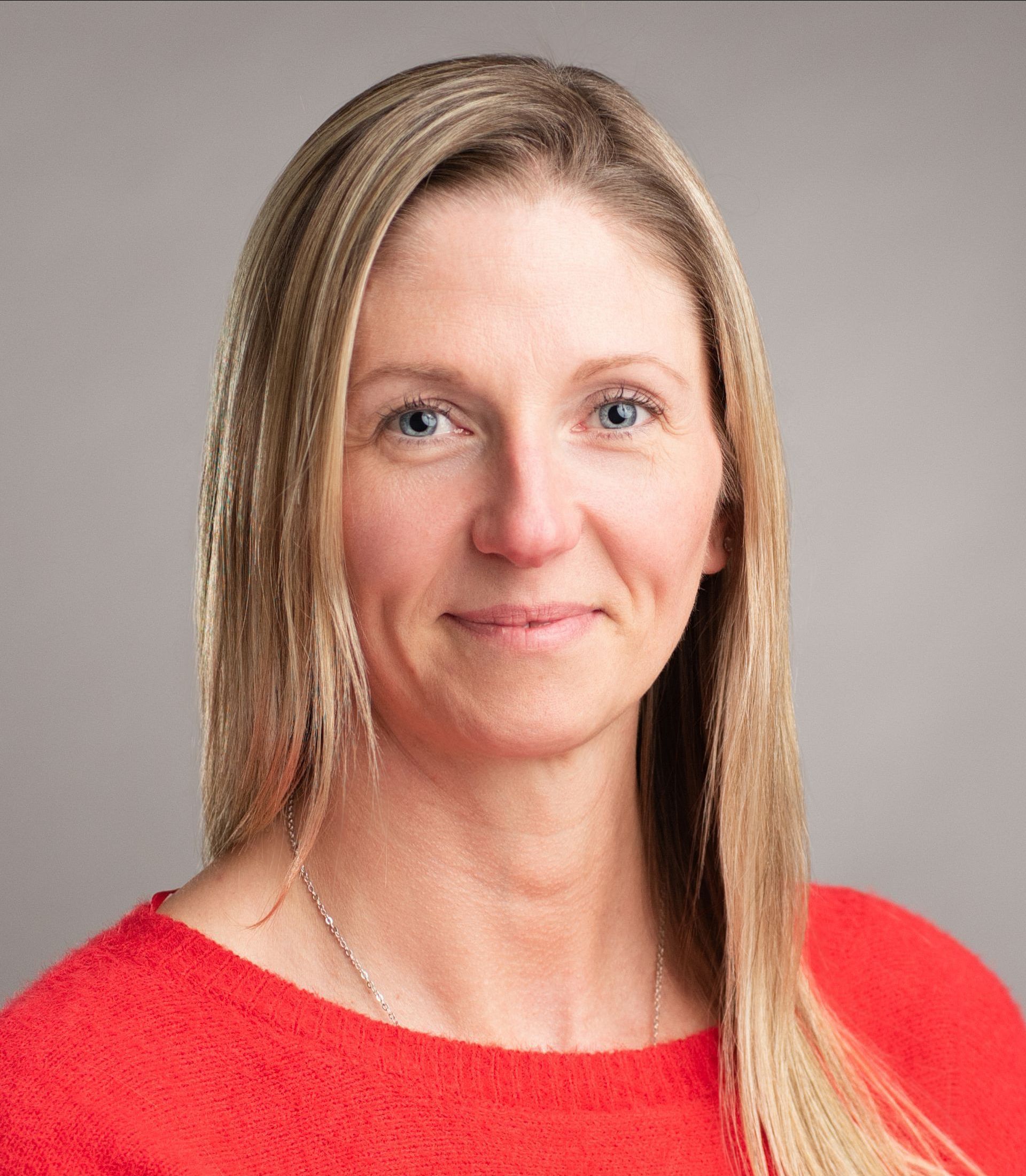 A woman is wearing a red sweater and smiling for the camera.
