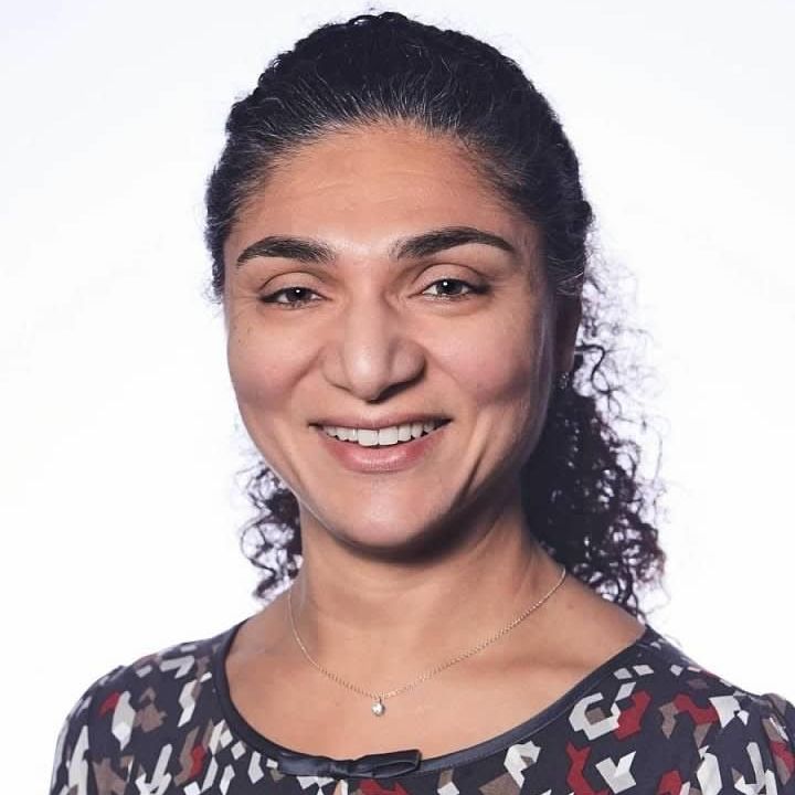 A woman with curly hair is smiling and wearing a necklace
