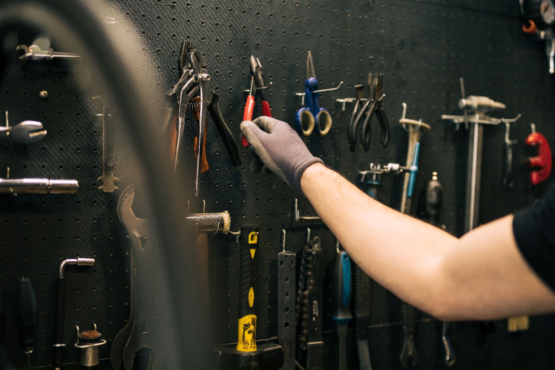 Una persona sostiene un par de alicates frente a una pared de herramientas.