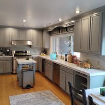 A kitchen with gray cabinets , stainless steel appliances , a table and chairs.