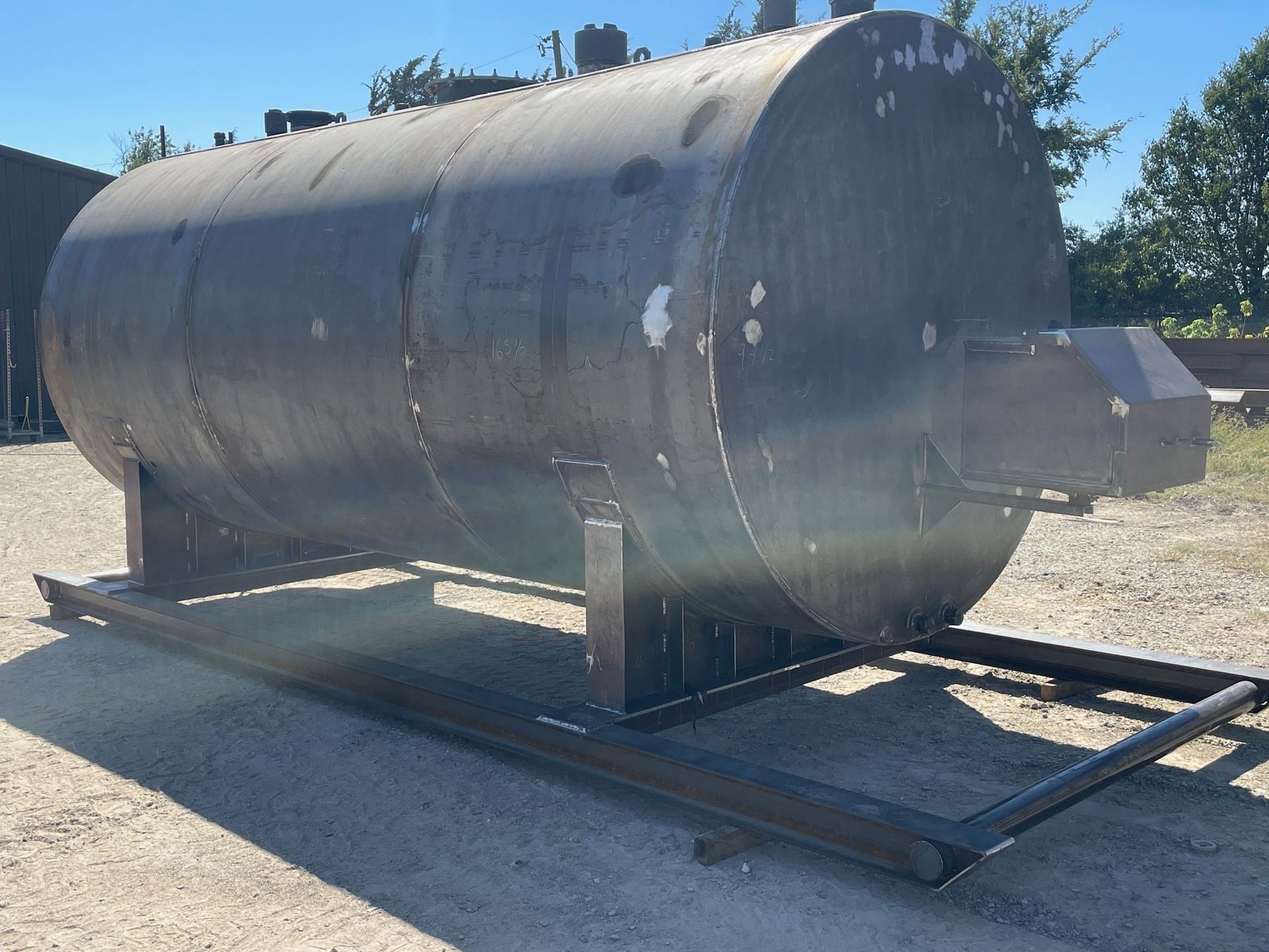 a large metal tank is sitting on a metal stand in a dirt lot .