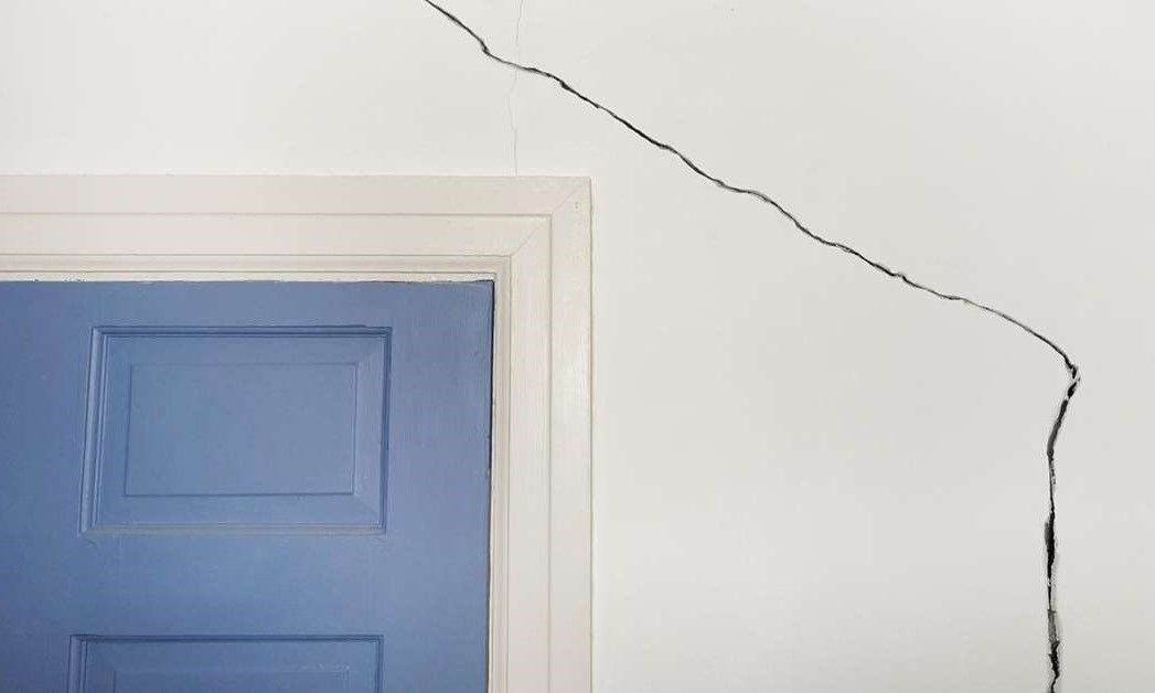 Blue door with white trim, a large crack extending up the white wall.