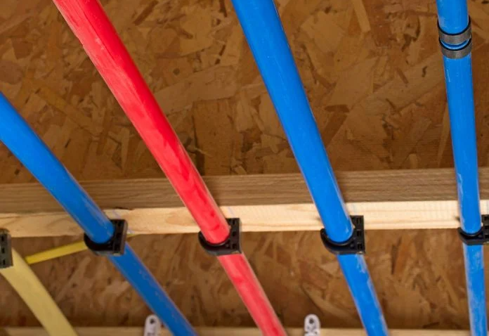 Blue and red water pipes secured to wood framing with black clips.