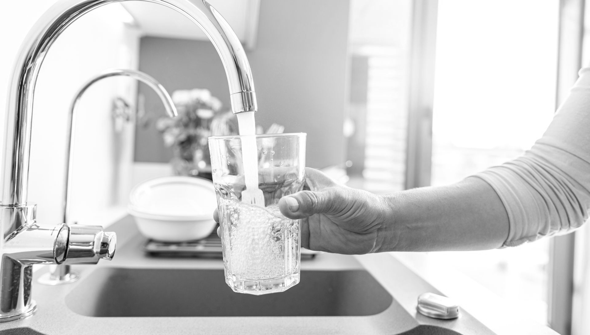 A hand holds a glass under a kitchen faucet, filling it with running water.
