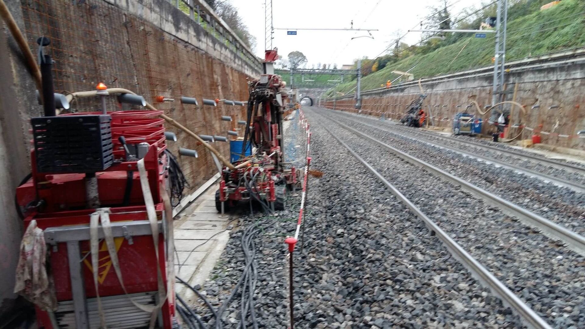 Una macchina rossa è parcheggiata sul ciglio dei binari del treno.