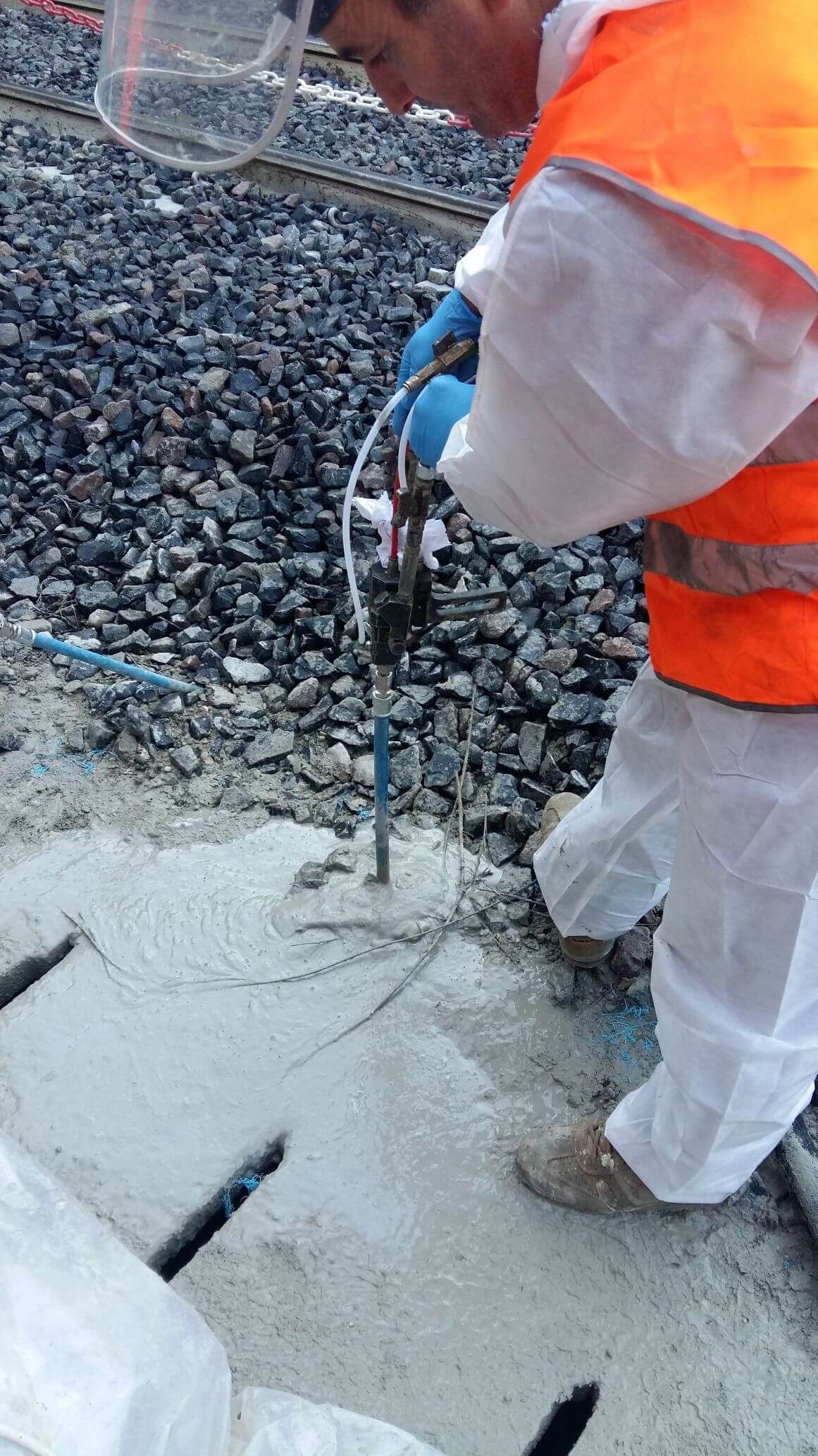 Un uomo con un gilet arancione e pantaloni bianchi sta lavorando su una superficie di cemento.