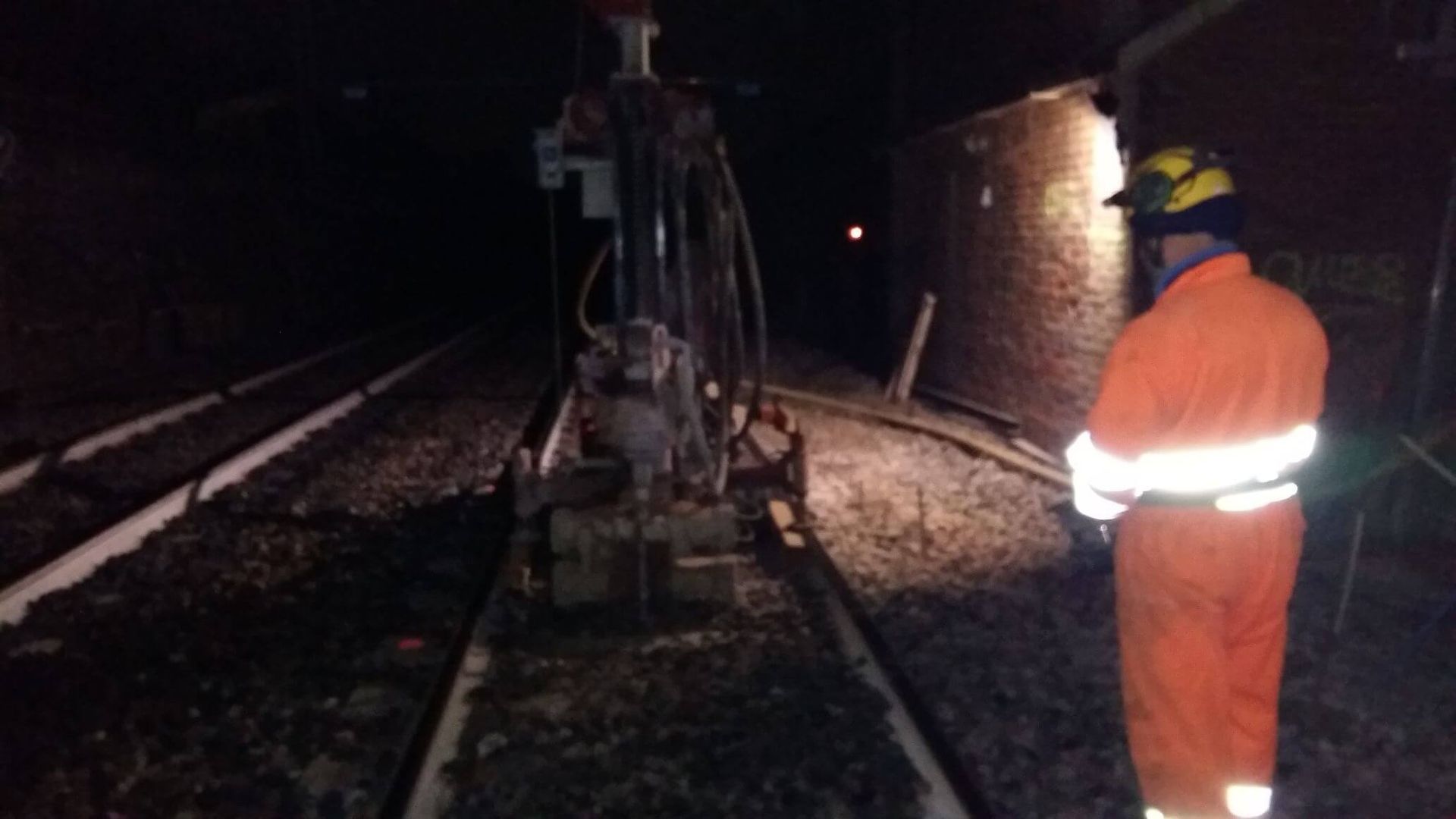 Un uomo con una tuta arancione è in piedi sui binari del treno di notte.