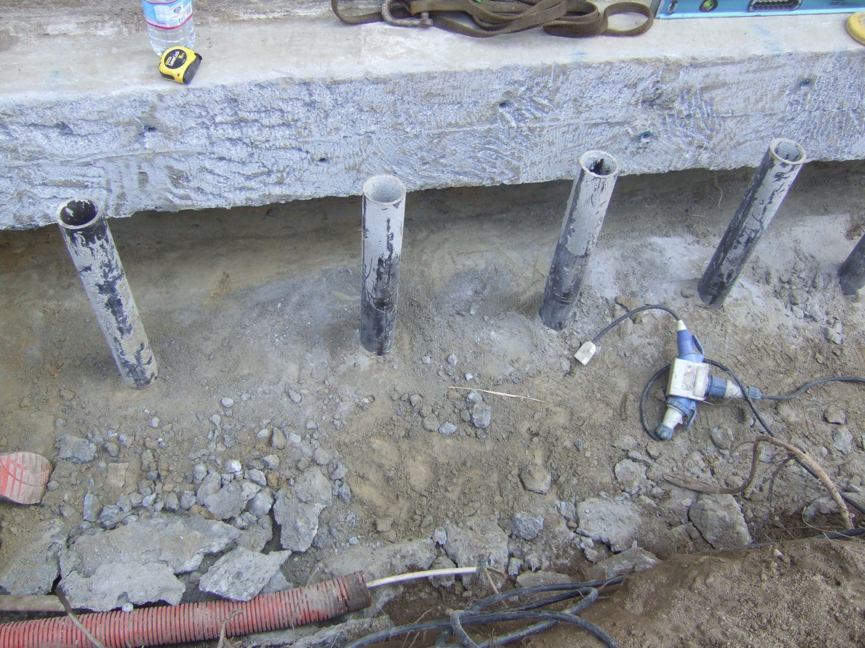 Un mucchio di tubi giace nella terra accanto a un muro di cemento.