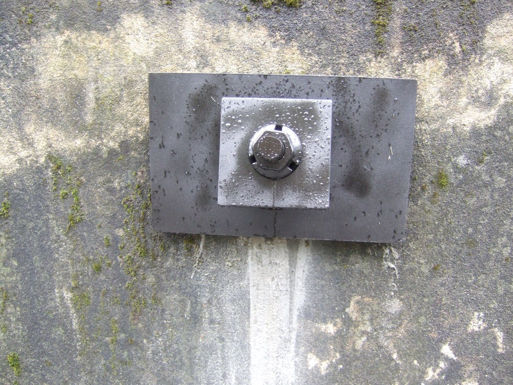Un pezzo di metallo con una vite è attaccato a un muro di cemento.