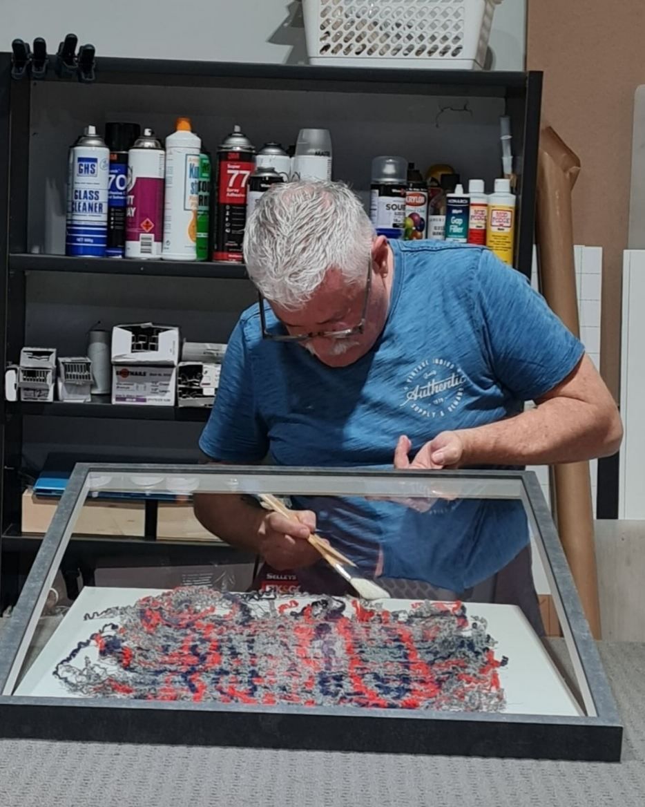 A Man in a Blue Shirt is Working on a Painting — Next Level Picture Framing In Ballina, NSW