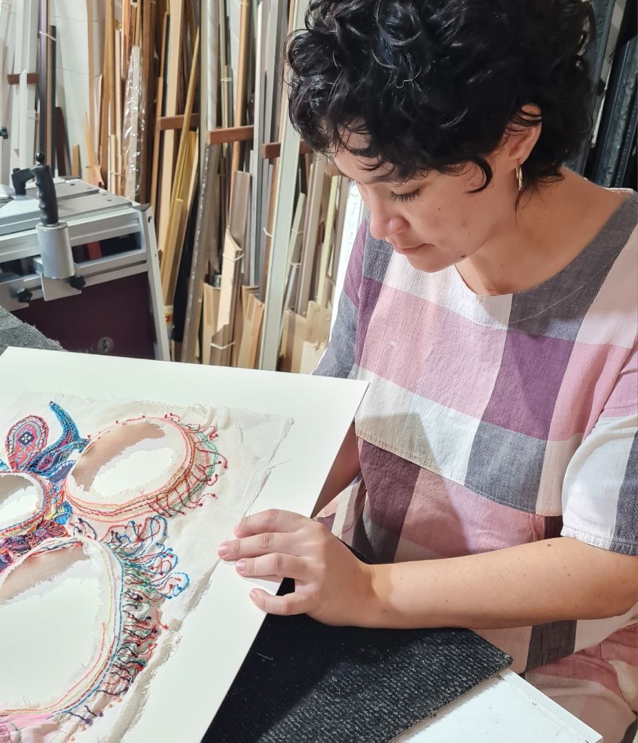 Woman With Dark Curly Hair Examines A Colorful Artwork — Next Level Picture Framing In Ballina, NSW