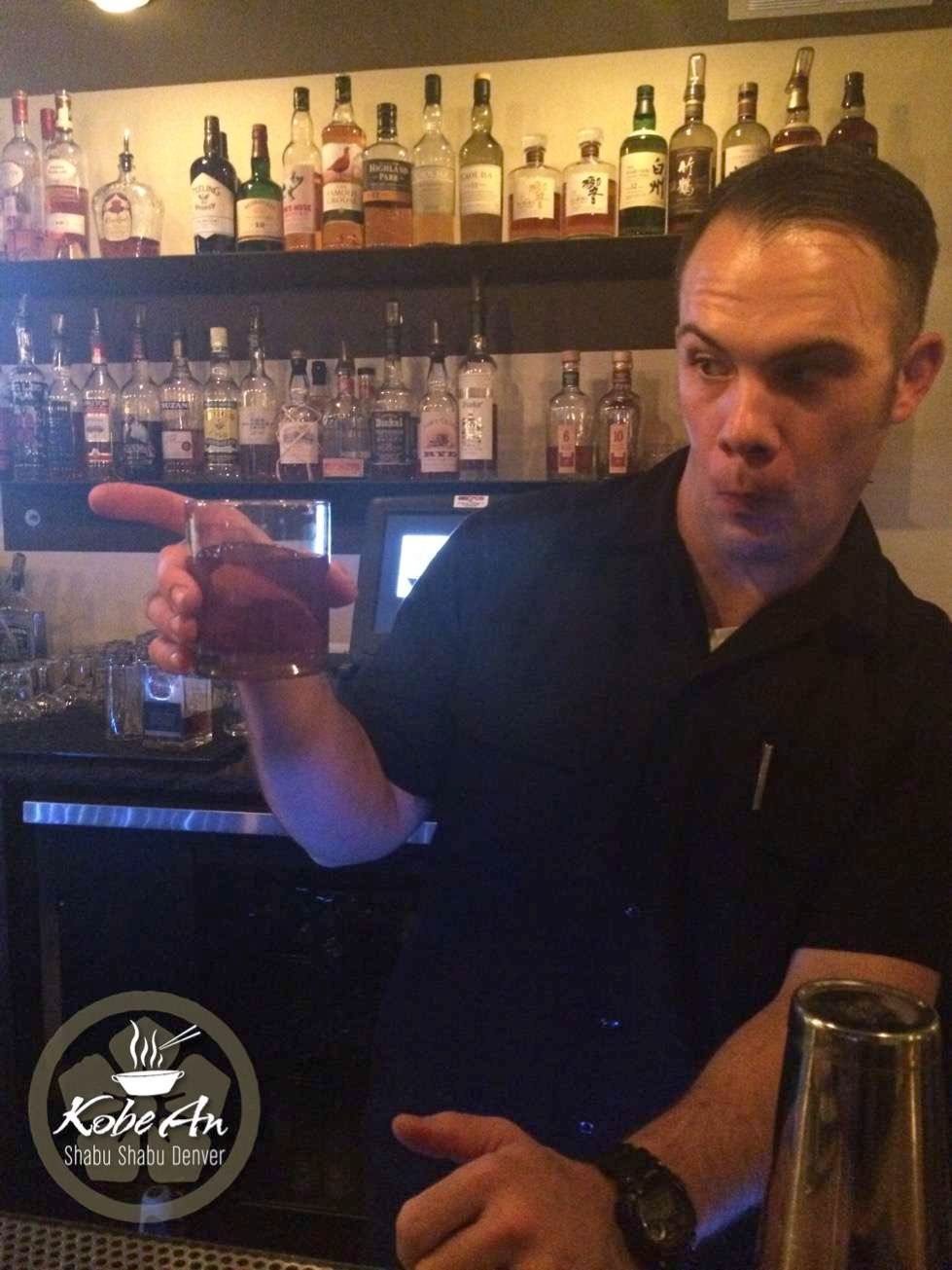 a bartender holds a glass in front of a shelf full of liquor bottles