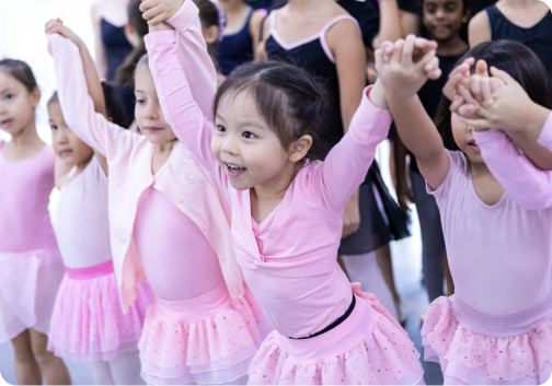 Image 2: A group of young girls in pink tutus are holding hands in a dance studio.