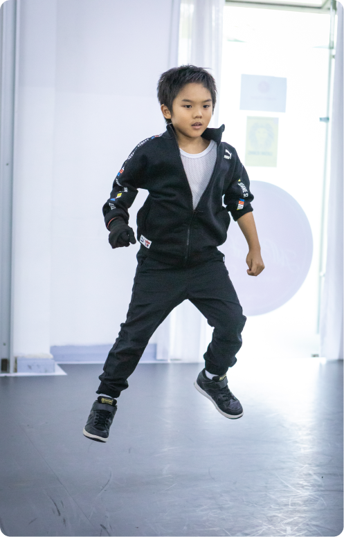 Image 5: A young boy in a black jacket and black pants is jumping in the air.