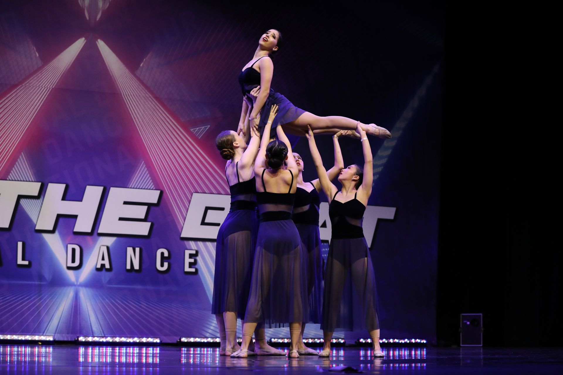 A group of dancers are performing on a stage in front of a sign that says the great dance