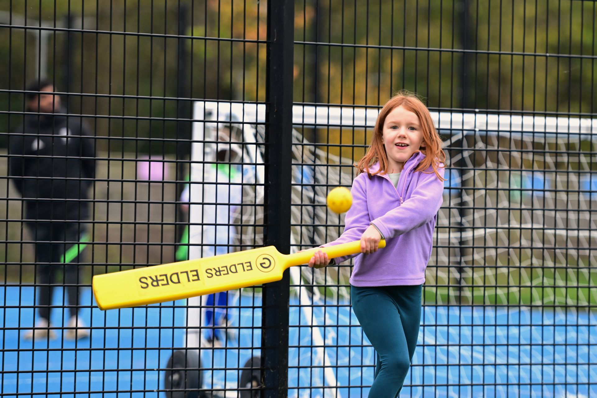 A teenage girl begins to throw a netball through a hoop whilst another girl tries to defend. They are wearing casual sports wear and the image is shot from a high angle view.