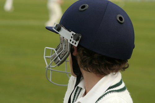 Young boy wearing a batsman,s helmet watches the team play