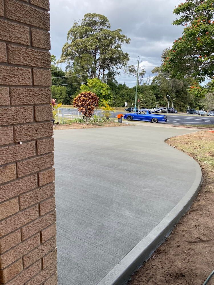 Newly Poured Concrete Driveway With a Brick Wall on the Left and a Blue Car — JDC Concreting in Grafton, NSW
