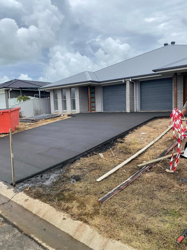 A Freshly Poured Concrete Driveway Leading to a Modern Gray House — JDC Concreting in Grafton, NSW