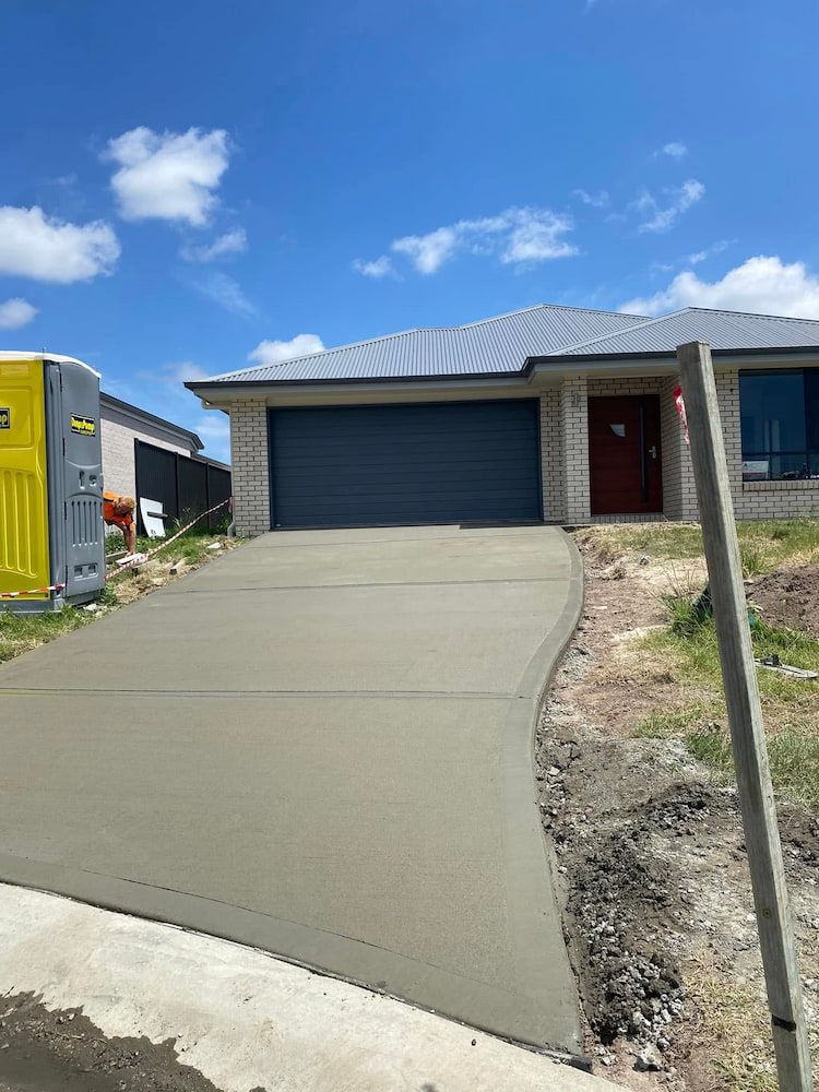 Newly Poured Concrete Driveway Leading Up to a Beige Brick House — JDC Concreting in Ballina, NSW