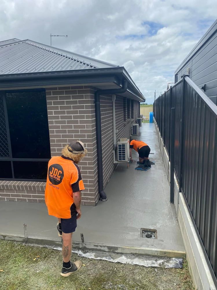 Two Workers in Orange Vests Are Working on Concrete Near a Brick Building — JDC Concreting in Grafton, NSW