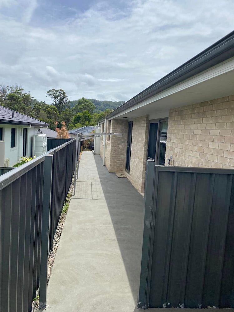 Narrow Concrete Walkway Between a Brick Building and a Black Metal Fence — JDC Concreting in Grafton, NSW