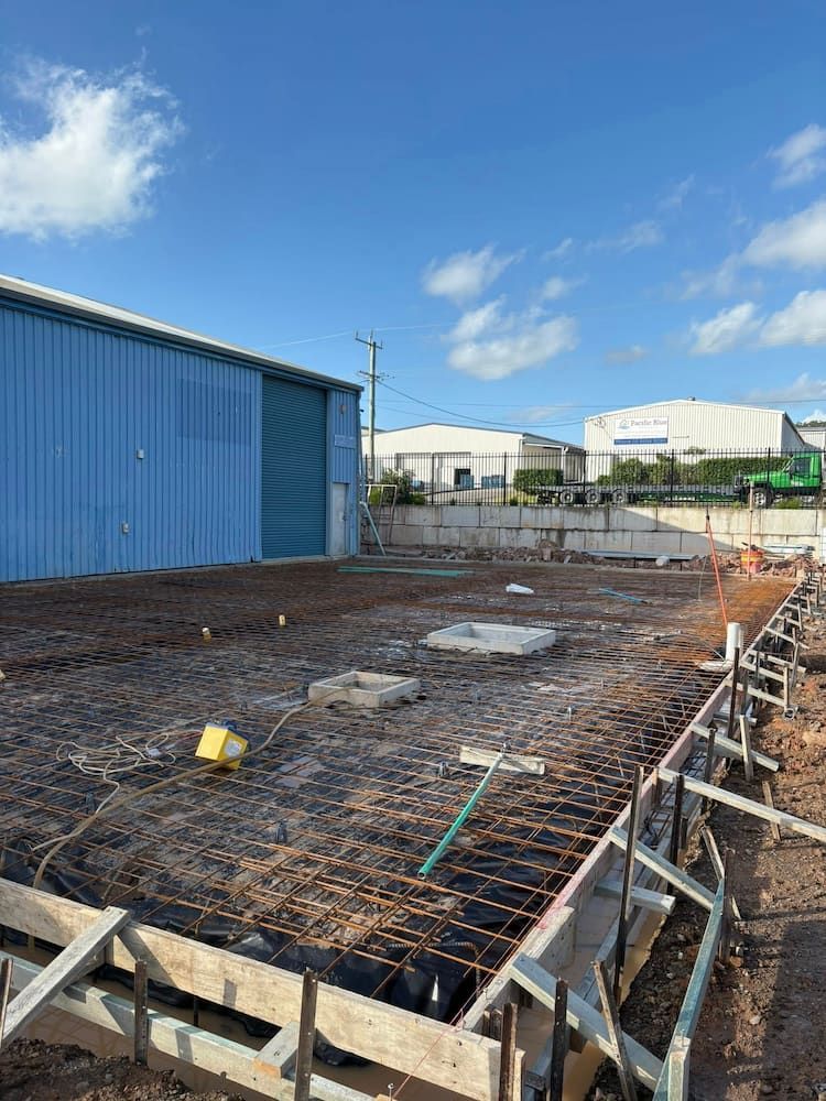 Construction Site With Rebar, Concrete Forms, and a Blue Metal Building — JDC Concreting in Grafton, NSW