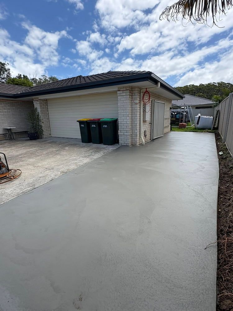 Freshly Poured Concrete Driveway in Front of a Brick Garage Under a Cloudy Sky — JDC Concreting in Grafton, NSW