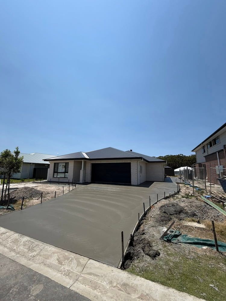 New Concrete Driveway Leading to a Modern House Under Construction — JDC Concreting in Ballina, NSW