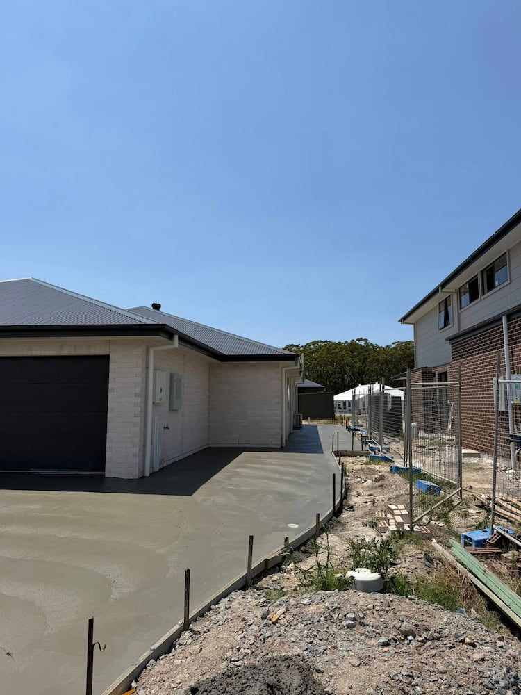 New Concrete Driveway Next to a Light-coloured House With a Dark Garage Door — JDC Concreting in Lismore, NSW
