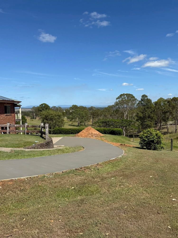 A Paved Driveway Curves Through a Grassy Lawn Toward a Pile of Mulch — JDC Concreting in Grafton, NSW