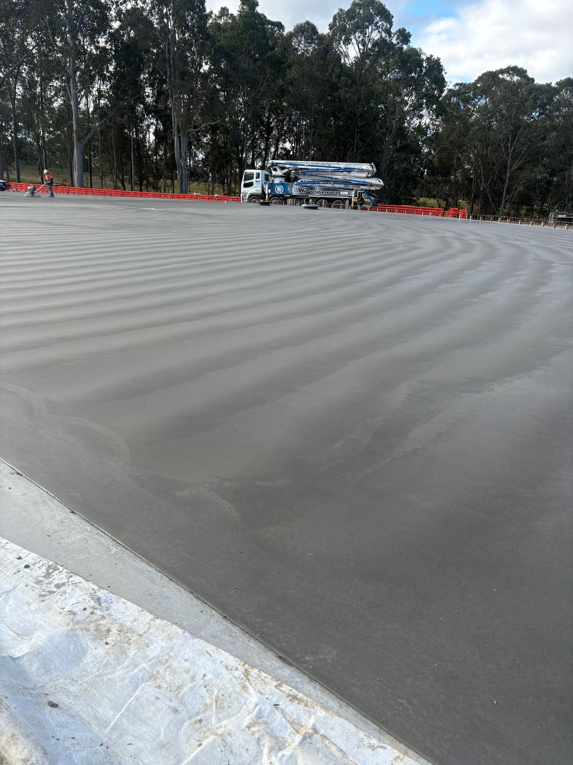 Newly poured concrete surface, with a truck and trees in the background — JDC Concreting in Ballina, NSW