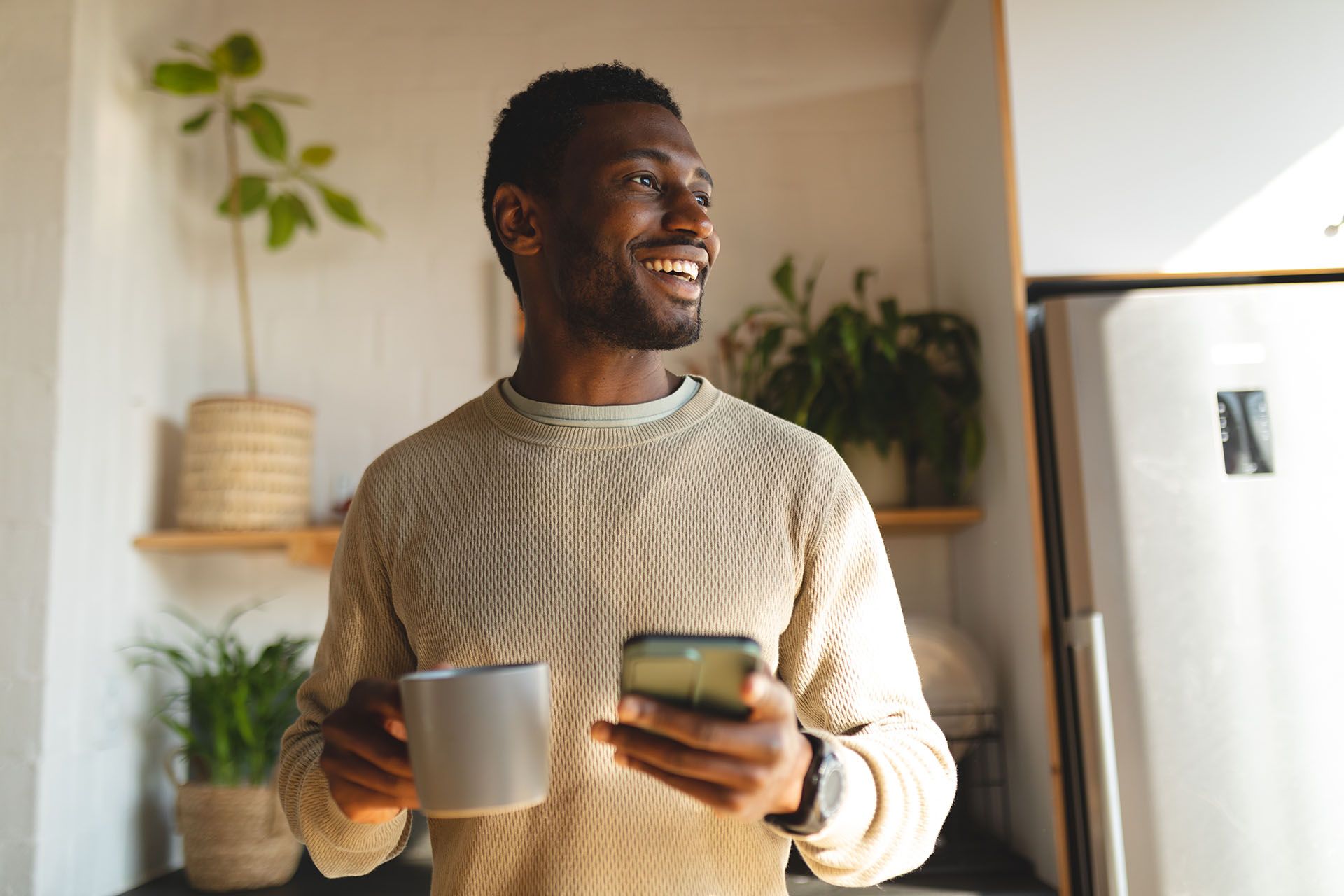 A man is holding a cup of coffee and a cell phone.