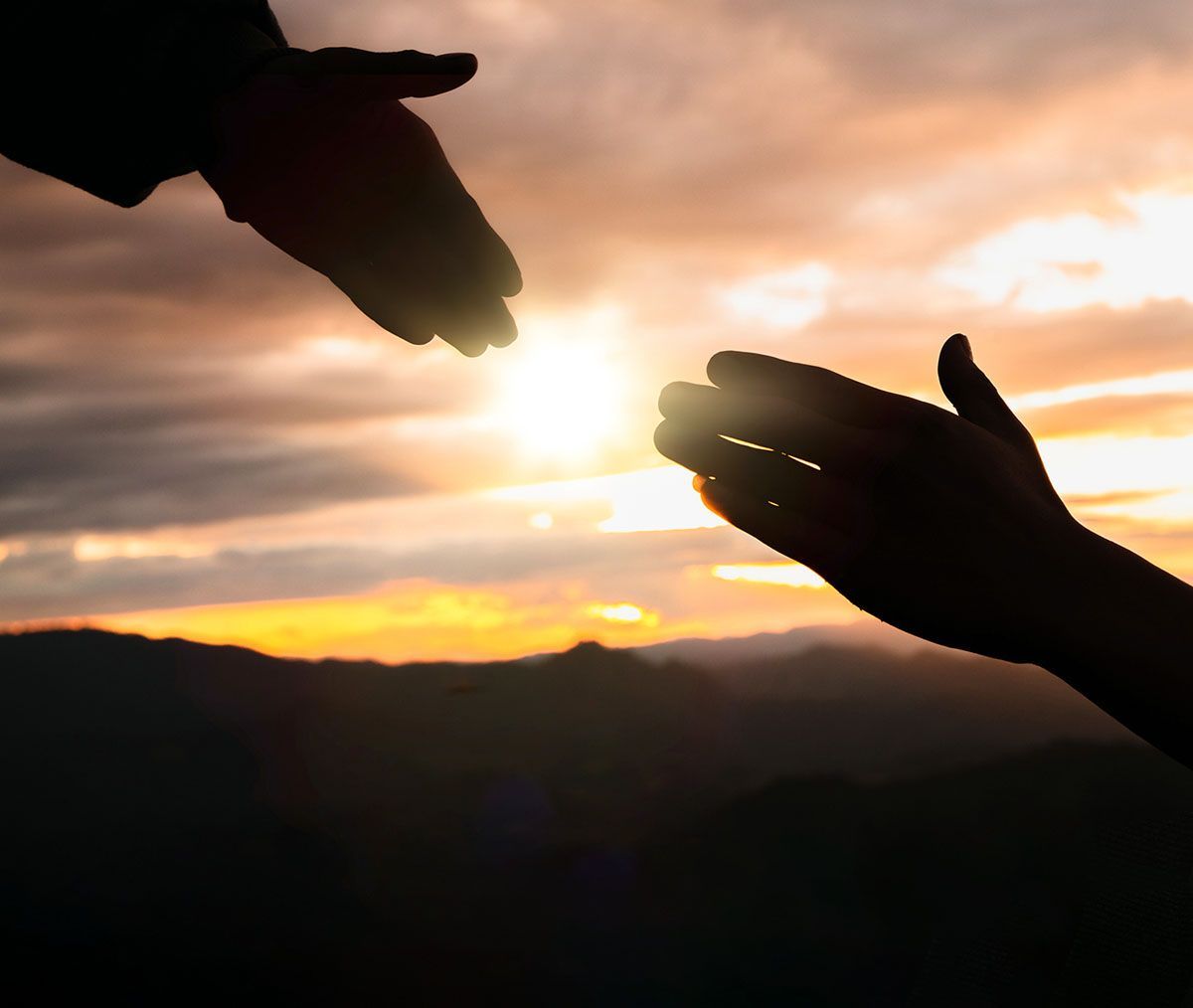 Two hands reaching out towards the sun at sunset.