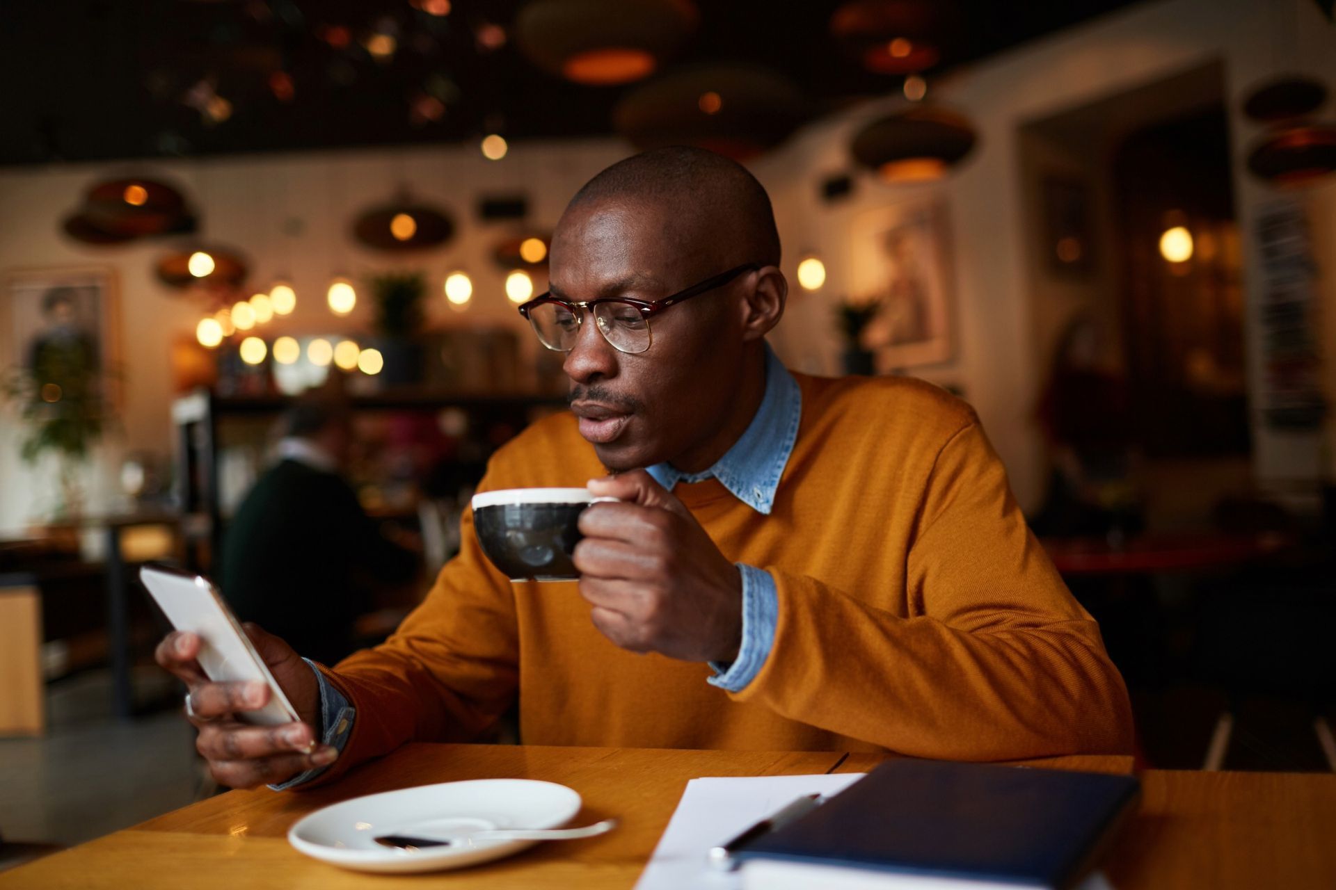 Man holding coffee and looking at tablet in a cafe.