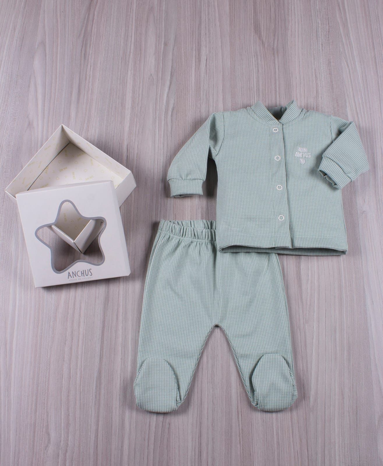 Conjunto de bebé a cuadros color menta con pantalón a juego junto a una tarjeta doblada sobre una superficie de madera.