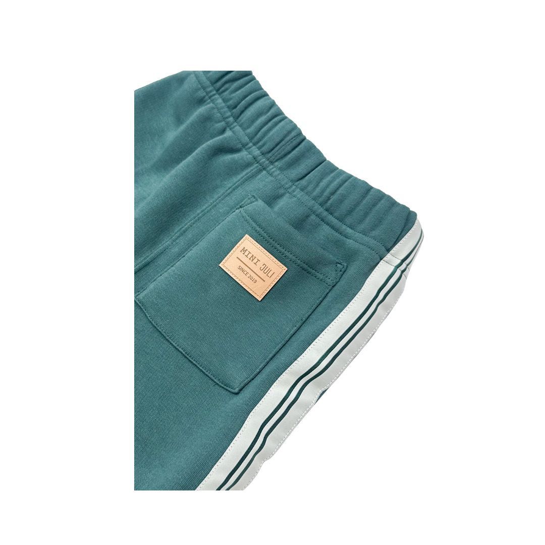 Pantalones verdes con cordón ajustable y rayas blancas en los laterales, con una pierna doblada para mostrar el puño.