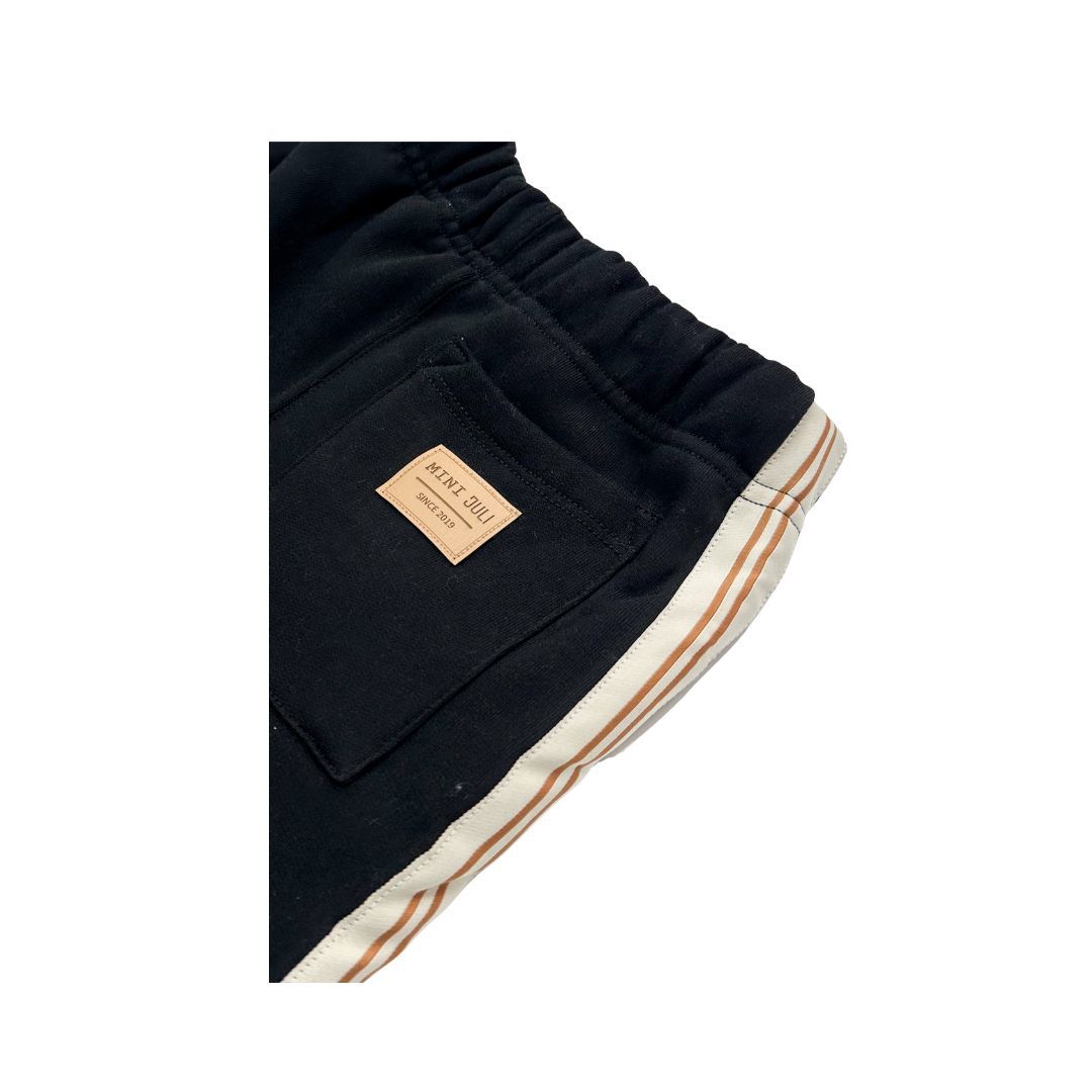 Pantalones deportivos negros con rayas laterales blancas y cordón ajustable sobre fondo blanco.