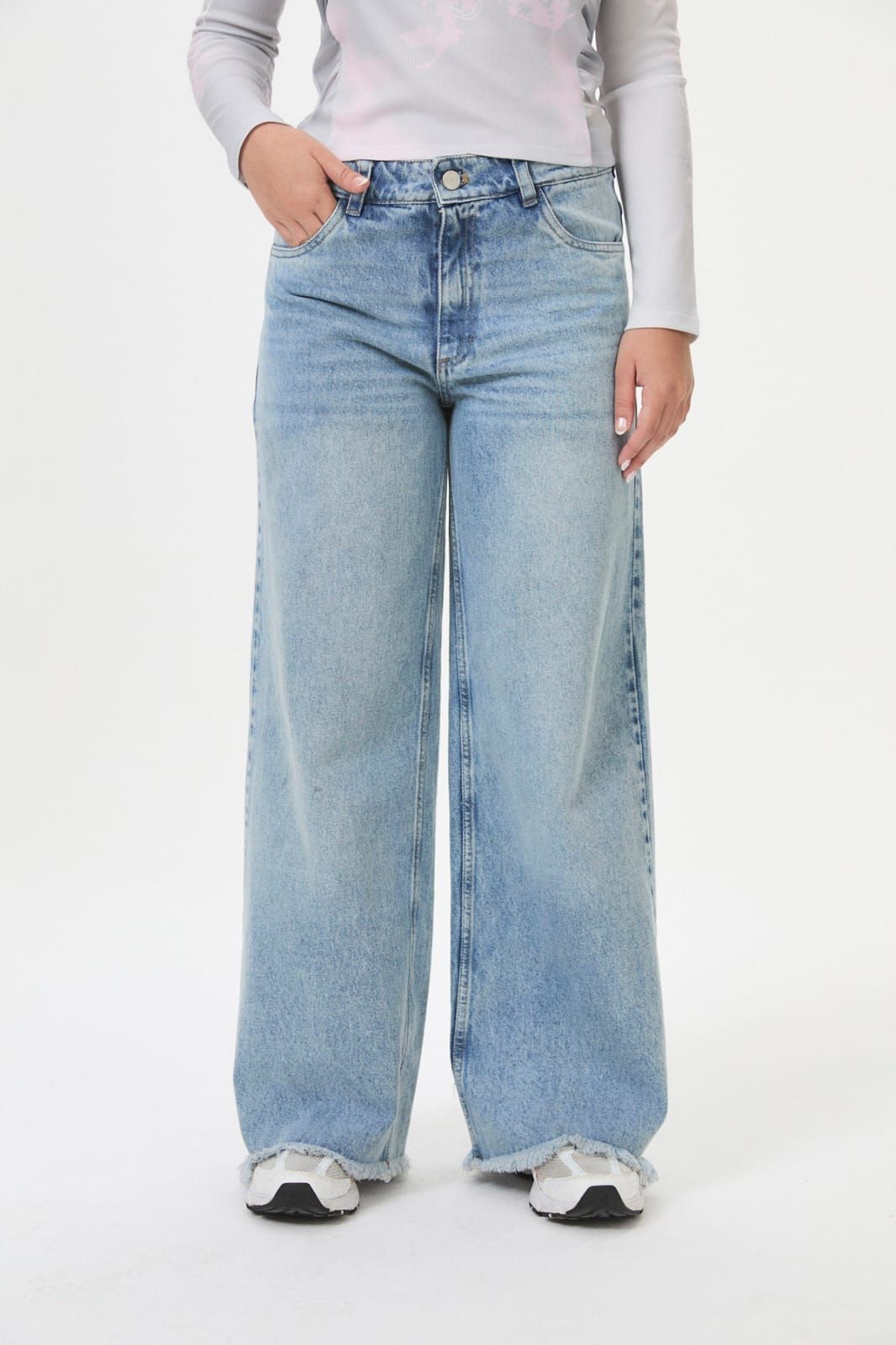 Persona con pantalones vaqueros anchos azul claro y zapatillas blancas sobre un fondo blanco.