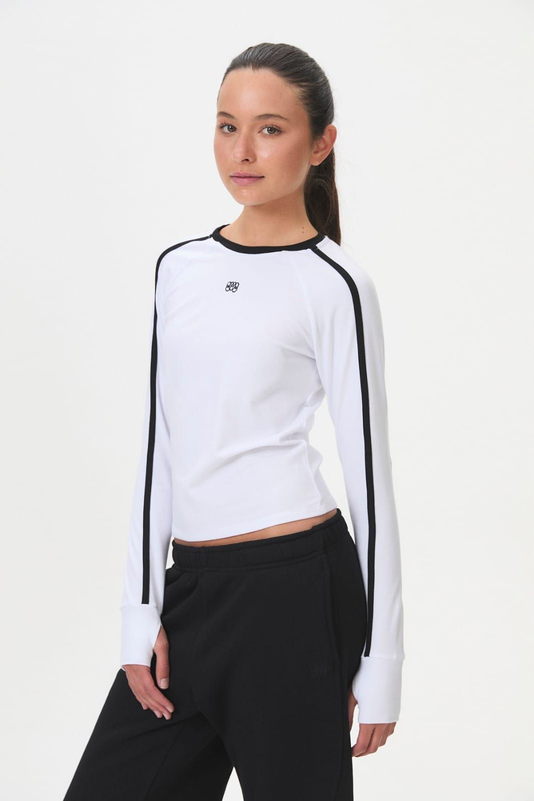 Mujer modelando una blusa blanca de manga larga con ribete negro y pantalones negros sobre un fondo liso.