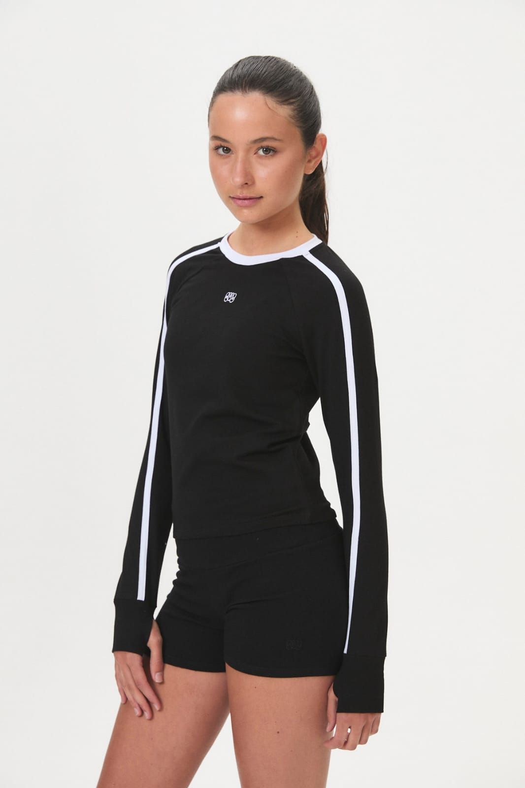 Mujer modelando una blusa blanca de manga larga con ribete negro y pantalones negros sobre un fondo liso.