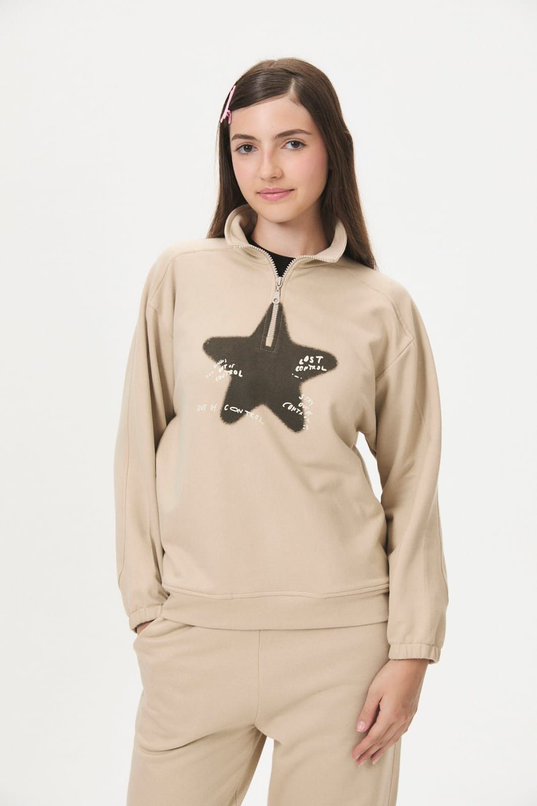 Mujer con sudadera rosa y pantalones con un gráfico de estrella negra, usando gafas de sol sobre un fondo blanco.