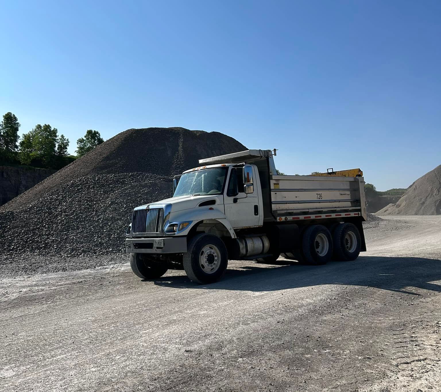A white dump truck is parked in front of a pile of gravel