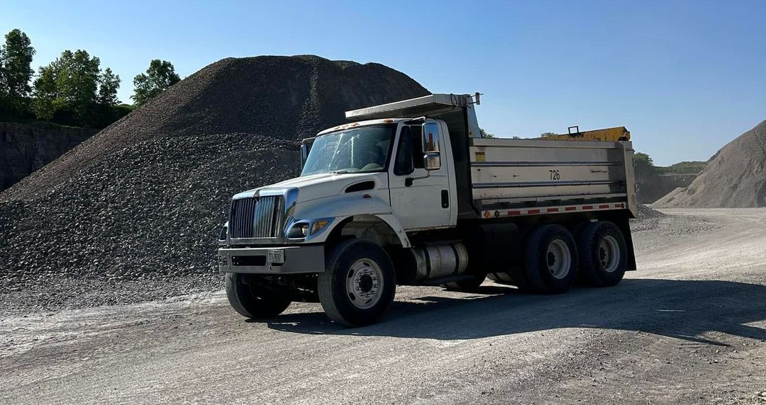A dump truck is parked in front of a pile of gravel.