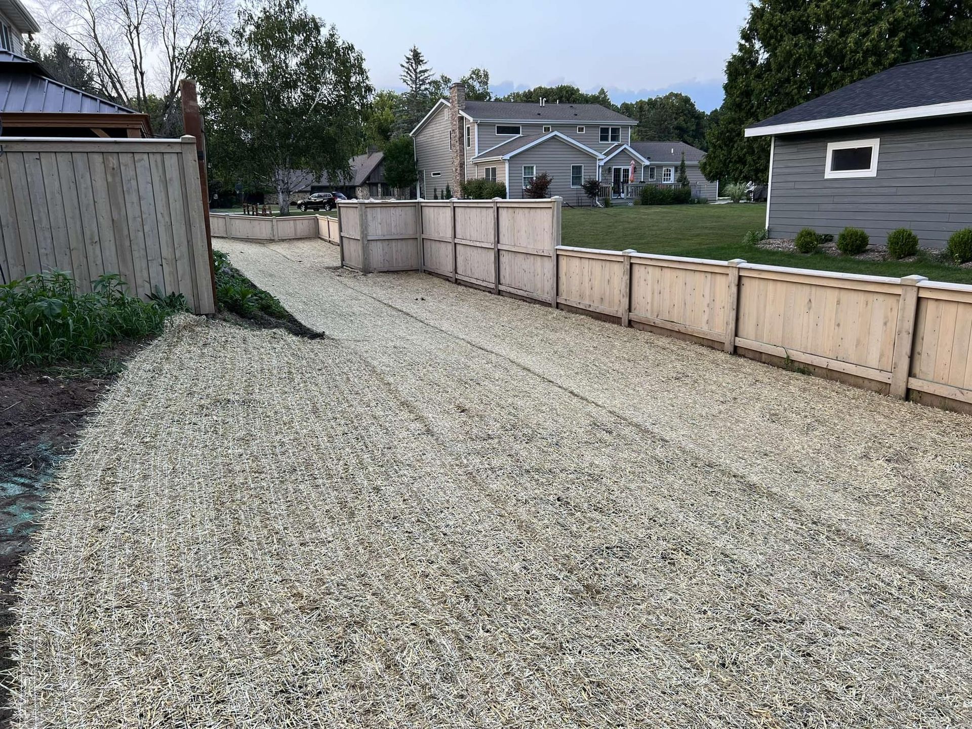 A gravel driveway leading to a house with a wooden fence.
