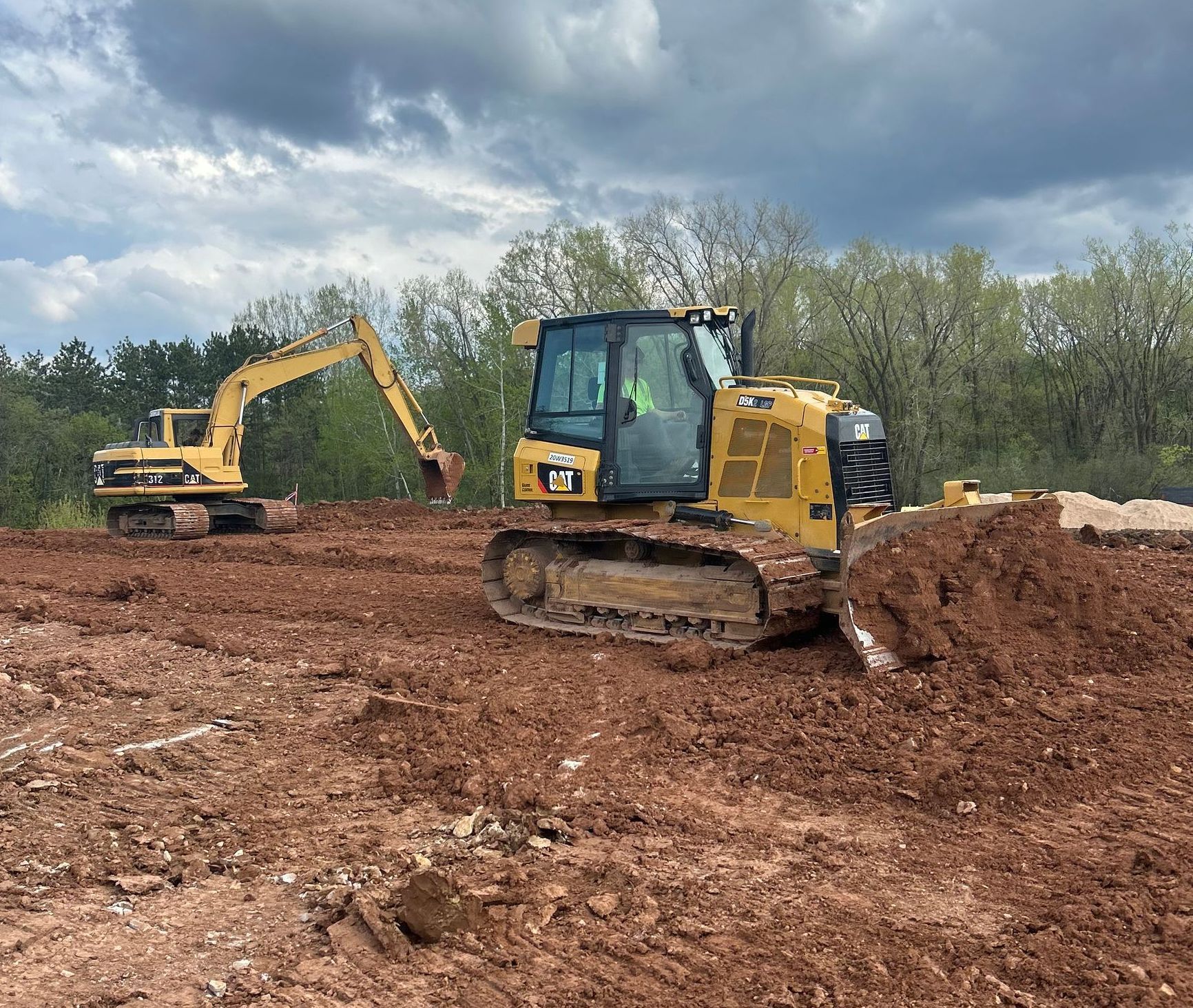 A bulldozer and an excavator are driving through a dirt field.