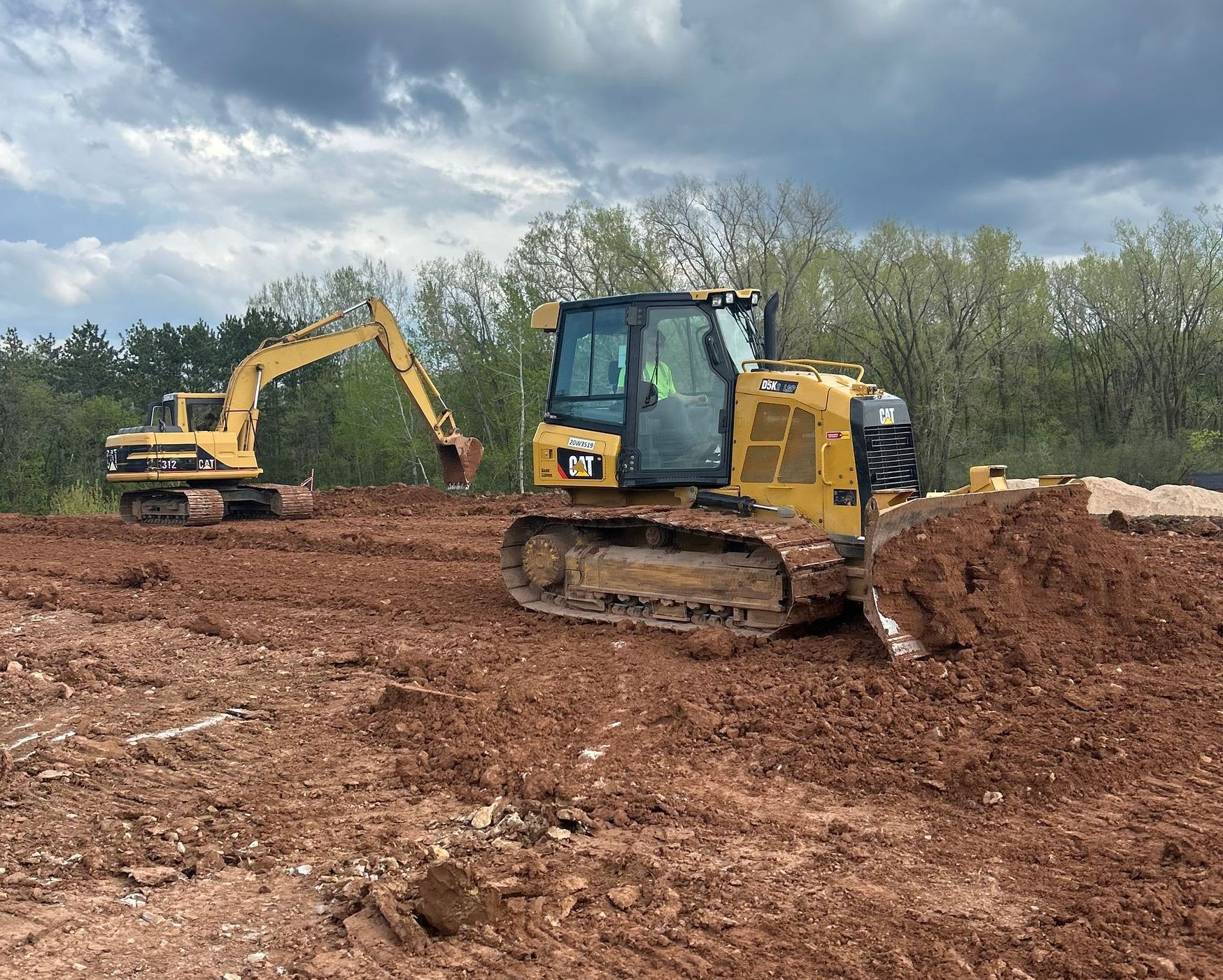 A bulldozer and an excavator are working in a dirt field.